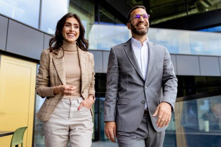 Photo for Two professionals exude confidence and happiness as they walk out of a contemporary office, reflecting success. - Royalty Free Image