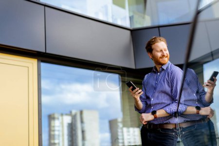 Foto de Un hombre enfocado en una camisa a rayas habla en su teléfono mientras domina el balcón a la luz del sol. - Imagen libre de derechos