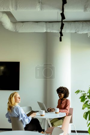 Foto de Dos colegas disfrutando de una alegre conversación sobre el café en un entorno de oficina soleado y moderno. - Imagen libre de derechos