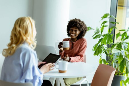 Photo for Two colleagues enjoying a cheerful conversation over coffee in a sunny, modern office setting. - Royalty Free Image