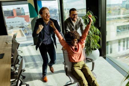 Photo for Exuberant co-workers engage in an impromptu office chair race, basking in the afternoon light with laughter. - Royalty Free Image