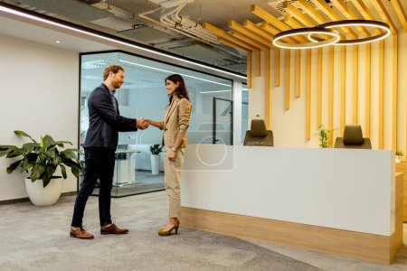 Foto de Dos profesionales intercambian saludos con un apretón de manos amigable en un ambiente de oficina elegante - Imagen libre de derechos