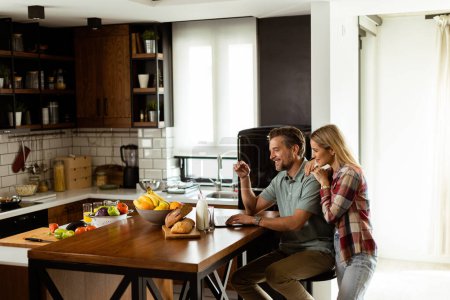 Photo for A cheerful couple enjoys a light-hearted moment in their sunny kitchen, working on laptop surrounded by a healthy breakfast - Royalty Free Image