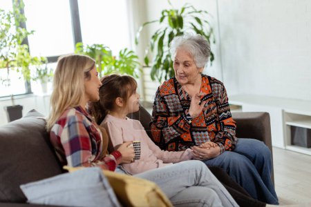 Drei Generationen von Frauen genießen Lachen und Gespräche auf einer gemütlichen Wohnzimmercouch