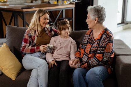 Foto de Tres generaciones de mujeres disfrutan de la risa y la conversación en un cómodo sofá de sala de estar - Imagen libre de derechos