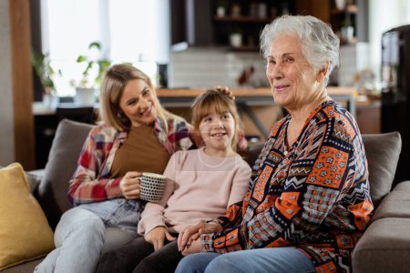 Téléchargez les photos : Trois générations de femmes aiment rire et converser sur un canapé confortable du salon - en image libre de droit