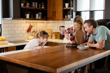 Téléchargez les photos : Une scène chaleureuse se déroule alors qu'une famille savoure un délicieux gâteau au chocolat dans la chaleur de sa cuisine ensoleillée, partageant des sourires et créant des souvenirs - en image libre de droit