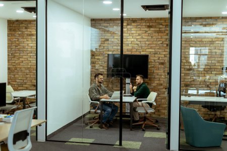 Dos profesionales conversan sentados cómodamente en un salón de oficina, rodeado de vegetación y elementos de diseño contemporáneo