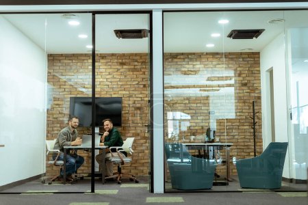 Zwei Profis führen ein Gespräch, während sie bequem in einer Bürolounge sitzen, umgeben von viel Grün und modernen Designelementen