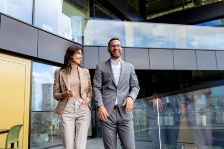 Two professionals exude confidence and happiness as they walk out of a contemporary office, reflecting success.