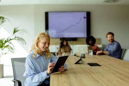 Téléchargez les photos : Joyeuse femme d'affaires tient une tablette numérique, avec un graphique de croissance à l'écran derrière, lors d'une réunion d'équipe réussie - en image libre de droit