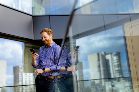 Téléchargez les photos : Un homme concentré dans une chemise rayée parle sur son téléphone tout en surplombant le balcon baigné de soleil. - en image libre de droit