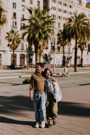 Foto de Pareja joven toma de la mano y sonríe mientras caminan por un sendero soleado en Barcelona, enmarcado por palmeras - Imagen libre de derechos