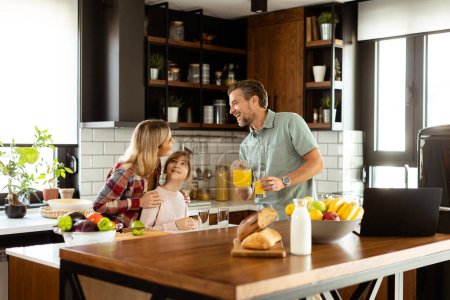 Photo for Young family chatting and preparing food around a bustling kitchen counter filled with fresh ingredients and cooking utensils - Royalty Free Image