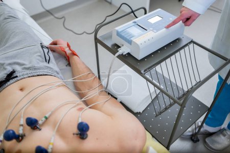 Téléchargez les photos : Un technicien surveille un test de tension cardiaque, avec des électrodes attachées à la poitrine d'un patient dans un cadre clinique. - en image libre de droit