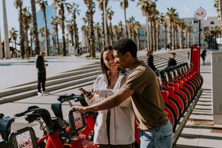 Photo for Young pair enjoying a breezy day choosing bikes from a rental station in Barcelona. - Royalty Free Image