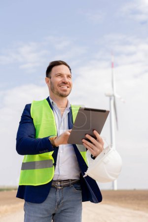 A professional with a tablet smiles optimistically at a wind farm