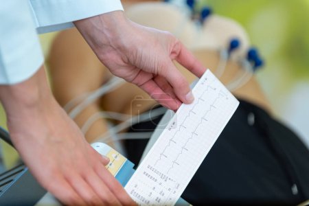 Téléchargez les photos : Un soignant vérifie attentivement les signes vitaux d'un patient avec une lecture EKG à la main. - en image libre de droit