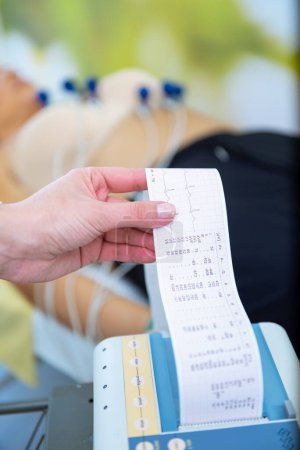 Un cuidador está revisando atentamente los signos vitales de un paciente con una lectura del electrocardiograma en la mano.