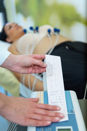 Foto de Un cuidador está revisando atentamente los signos vitales de un paciente con una lectura del electrocardiograma en la mano. - Imagen libre de derechos