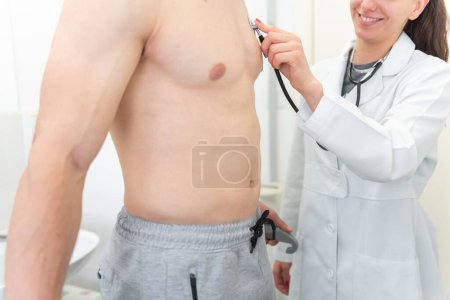 Un médecin souriant utilise un stéthoscope pour écouter la poitrine d'un patient dans une clinique médicale.