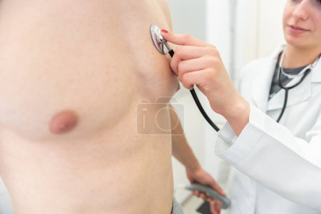 Téléchargez les photos : Un médecin souriant utilise un stéthoscope pour écouter la poitrine d'un patient dans une clinique médicale. - en image libre de droit