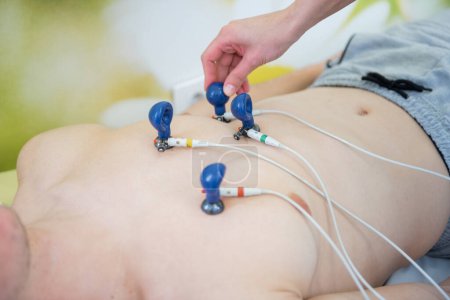 Téléchargez les photos : Praticien qualifié attache soigneusement électrodes EKG à un patient pour la surveillance cardiaque - en image libre de droit