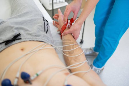 Téléchargez les photos : Praticien qualifié attache soigneusement électrodes EKG à un patient pour la surveillance cardiaque - en image libre de droit