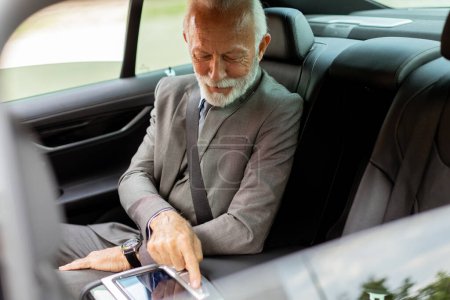 Distinguido hombre mayor en un traje ajusta el panel de control de pantalla táctil de un vehículo de lujo mientras viaja.