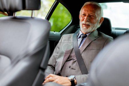 Photo for Well-dressed elderly man with a beard smiles contentedly while seated in the back of a modern vehicle - Royalty Free Image