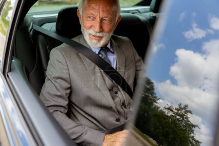Téléchargez les photos : Un homme âgé avec une barbe portant un costume et une cravate, attaché avec une ceinture de sécurité, regardant contenu dans son véhicule - en image libre de droit