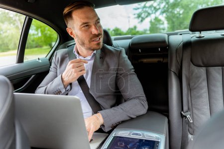 Photo for Focused man in business attire typing on a laptop in the backseat of a car, harnessing every minute - Royalty Free Image