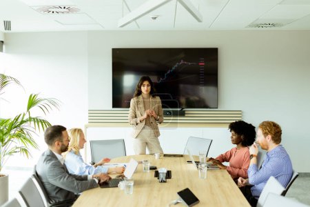 Téléchargez les photos : La femme d'affaires souligne les tendances de croissance sur un écran lors d'une réunion financière, les participants écoutant attentivement - en image libre de droit
