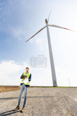 A professional with a digital tablet smiles optimistically at a wind farm