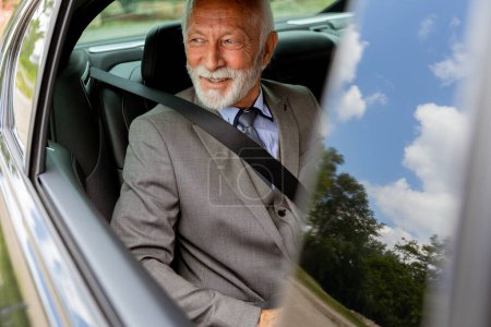 Ein älterer Mann mit Bart, Anzug und Krawatte, gesichert mit Sicherheitsgurt, schaut zufrieden in sein Fahrzeug