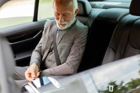 Distinguido hombre mayor en un traje ajusta el panel de control de pantalla táctil de un vehículo de lujo mientras viaja.