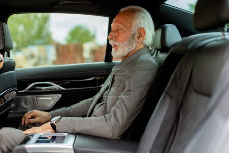 Foto de Un anciano bien vestido con barba sonríe contento mientras está sentado en la parte trasera de un vehículo moderno - Imagen libre de derechos