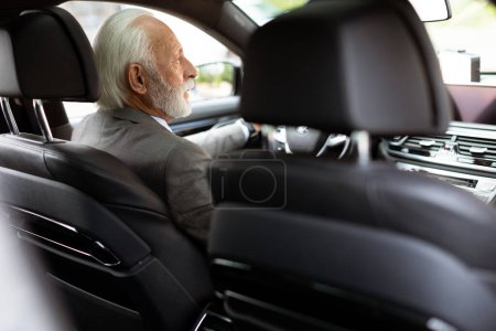 An elderly gentleman, dressed in a suit, confidently drives a modern car through a bustling city street on a bright, sunny day