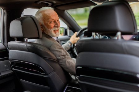An elderly gentleman, dressed in a suit, confidently drives a modern car through a bustling city street on a bright, sunny day