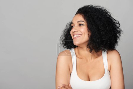 Feliz chica de raza mixta sonriente mirando a un lado en el espacio de copia en blanco, retrato de estudio sobre fondo gris