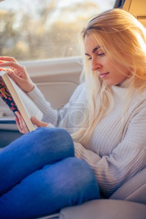 Téléchargez les photos : Blonde femme lire un livre dans la voiture sur la route - en image libre de droit