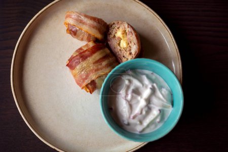 Téléchargez les photos : Délice salé : délicieux plat aux boulettes de viande enveloppées dans du bacon, rempli de mozzarella et de sauce au yaourt - en image libre de droit