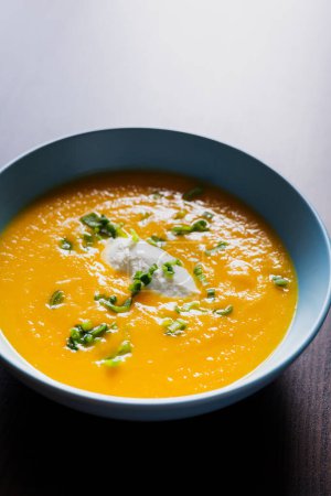 Photo for Delicious carrot soup in a bowl with cream and green onion close-up - Royalty Free Image