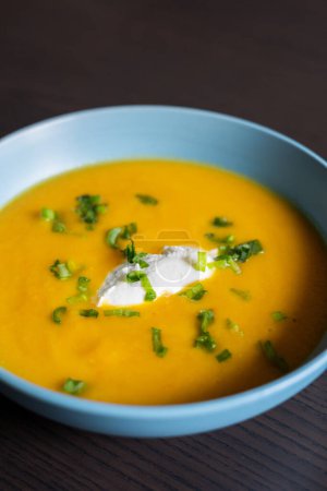 Téléchargez les photos : Délicieuse soupe aux carottes dans un bol avec crème et oignon vert close-up - en image libre de droit
