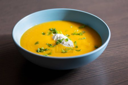 Photo for Delicious carrot soup in a bowl with cream and green onion close-up - Royalty Free Image