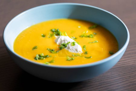 délicieuse soupe aux carottes dans un bol avec crème et oignon vert close-up