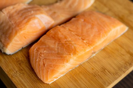  Close-up of raw, fresh salmon fillets arranged neatly on a wooden cutting board, showcasing their vibrant colors and textures