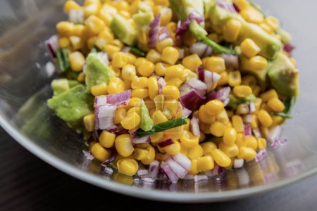 Photo for Vibrant colors of a summer salad featuring corn, red onion, and avocado, drizzled with lime dressing, presented in a glass bowl in this closeup - Royalty Free Image