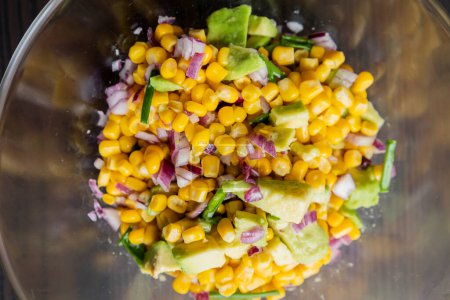 Photo for Vibrant colors of a summer salad featuring corn, red onion, and avocado, drizzled with lime dressing, presented in a glass bowl in this closeup - Royalty Free Image