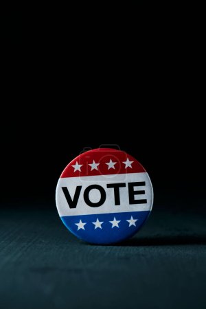primer plano de una insignia para las elecciones de Estados Unidos, con el voto de texto escrito en ella, sobre una superficie gris oscura, con un poco de espacio en blanco en la parte superior